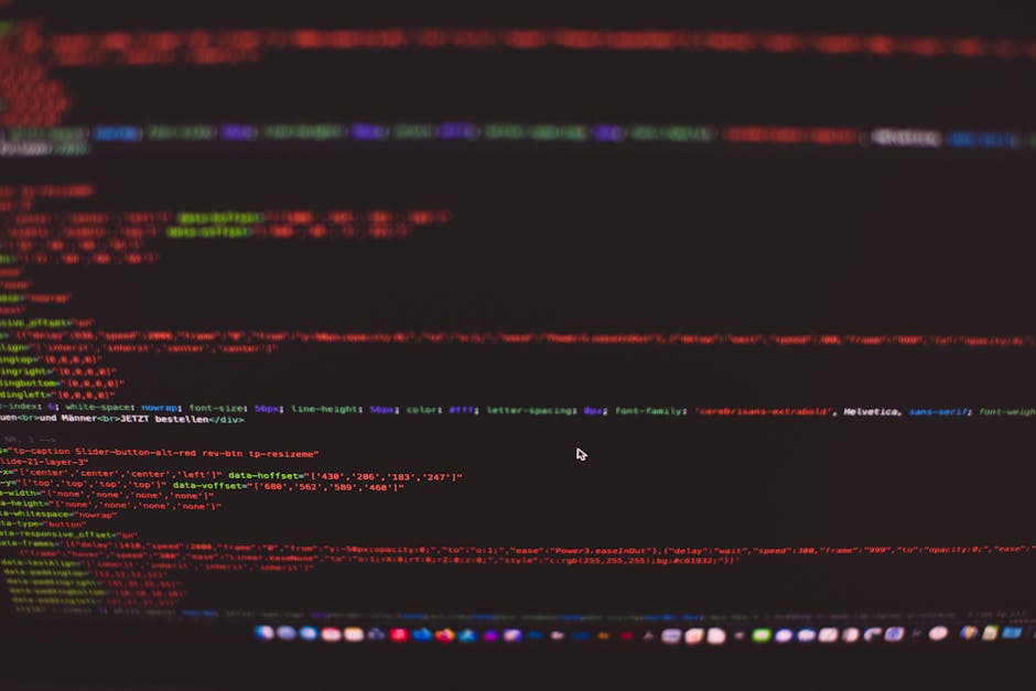 A person working at a desk with dual computer monitors displaying lines of code in a dimly lit room. The workspace features a wooden desk surface with a black keyboard and mouse, and a small satellite